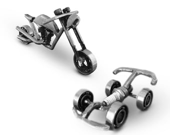 Puede incluir: Dos motocicletas en miniatura hechas de tuercas, tornillos y otros herrajes metálicos. La motocicleta más grande es de estilo chopper con una sola rueda delantera. La motocicleta más pequeña es de estilo karting con cuatro ruedas.