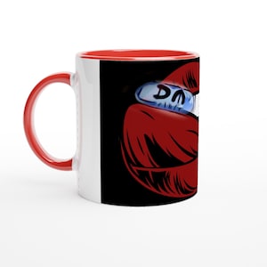 Könnte beinhalten: Eine weiße Keramiktasse mit rotem Griff und Innenraum. Die Tasse zeigt eine Grafik roter Lippen und eine blaue Pille mit den Buchstaben "DM". Der Hintergrund ist schwarz.
