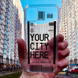 以下が含まれることがあります： 「YOUR CITY HERE」と書いてある黒と白のデザインの透明な携帯電話ケース。バーコードと「ISBN 978 90128 YCH ARRIVALS FIRST CLASS/PREMIERE CLASSE around the world」というテキストがあります。