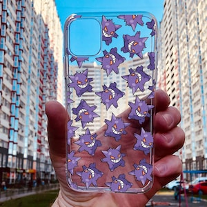 May include: A clear phone case with a purple and white pattern of a cartoon character with a menacing expression. The character is repeated throughout the case.