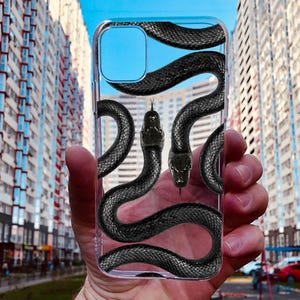 May include: A clear phone case featuring a black snake design. The snake is wrapped around the case with its head visible at the top.