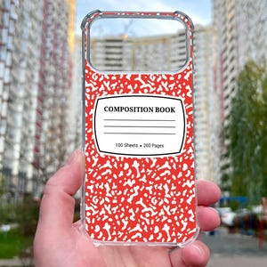 May include: A clear phone case featuring a red and white speckled pattern reminiscent of a composition notebook cover. The center displays a white label with the black text COMPOSITION BOOK, three horizontal lines, and 100 Sheets 200 Pages.