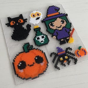 Puede incluir: Colección de arte de cuentas con temática de Halloween. Incluye un gato negro, un fantasma, una botella de poción, una bruja, una calabaza, una araña y una calabaza pequeña. Las figuras están hechas con cuentas de colores.