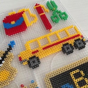 May include: A close-up of a colorful bead art project featuring a school bus, a fire extinguisher, scissors, and other school supplies. The beads are arranged in a grid pattern on a clear plastic board.