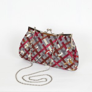 May include: A gray clutch with a silver chain strap. The clutch features a woven pattern in shades of gray, burgundy, and brown. The clasp is silver. The bag is approximately 10 inches wide and 6 inches tall.