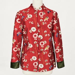 May include: A red long-sleeved jacket featuring a mandarin collar, three fabric-covered buttons, and a floral pattern with white and pink blossoms, green branches, and colorful butterflies. The sleeve cuffs are a solid dark olive green.