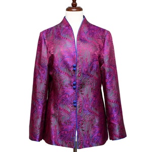 Op de afbeelding: Een paars en groen brokaatjasje met een mandarijnskraag en blauwe knopen. Het jasje heeft een pauwenveerpatroon.