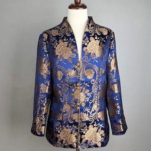 Pode incluir: Casaco azul com um padrão floral dourado. O casaco tem gola mandarim e botões dourados. O tecido tem brilho e o design floral é detalhado. O casaco é exibido em um manequim.