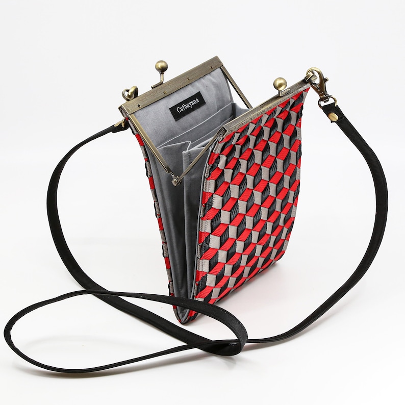 May include: A red and black woven crossbody bag with a silver clasp and a black adjustable strap. The bag is open and the interior is lined with gray fabric. The bag has a label that says "Cathayana".