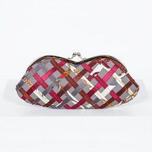 Può includere: Una pochette in tessuto grigio e rosso intrecciato con una chiusura a scatto argentata. La pochette ha un motivo floreale ed è realizzata in un tessuto morbido.