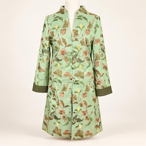May include: A light green long-sleeve coat featuring a repeating floral and butterfly embroidery pattern in shades of pink, yellow, and brown. The coat has a V-neckline, a front button closure with four visible buttons, and dark green cuffs.