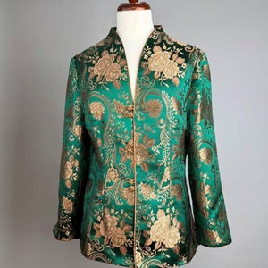 May include: Emerald green jacket with gold floral brocade pattern. The jacket features a mandarin collar, long sleeves, and decorative gold buttons. The fabric has a subtle sheen, adding to its elegant appearance.