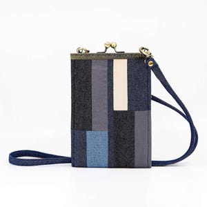 May include: A rectangular patchwork crossbody bag with a metal clasp closure and a denim strap. The bag features a geometric pattern of blue, gray, and off-white fabric blocks. The bag is approximately 7 inches tall and 4 inches wide.