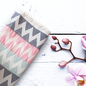 May include: A pink and gray patterned throw blanket with a chevron design, lying on a white wooden surface with pink orchid flowers.