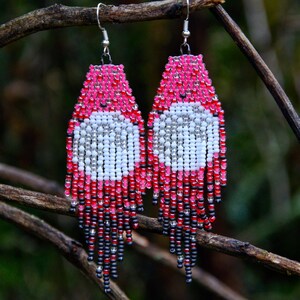 May include: Pink, white, and black beaded earrings with a unique design. The earrings are hanging from a branch, with the text "Dragonfly Earrings" and "ART FOR YOUR EARS" at the bottom.