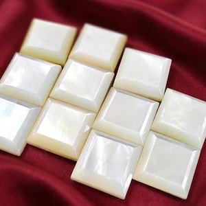 May include: A collection of nine square-shaped buttons crafted from iridescent mother-of-pearl. Each button features a smooth, beveled edge and a polished, reflective surface that displays a subtle, pearlescent white sheen across the material.