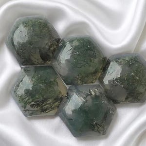 May include: Five hexagonal, polished stones with a translucent, light grey base and deep green, moss-like inclusions. Each stone features faceted edges and a smooth, glossy surface, displaying unique, organic patterns of dark green mineral deposits.