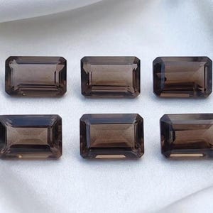 Puede incluir: Seis piedras preciosas de cuarzo ahumado, de forma rectangular y facetadas, dispuestas en dos filas de tres. Cada piedra presenta un tono marrón profundo y transparente con cortes geométricos precisos y bordes definidos.
