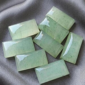 May include: A collection of seven rectangular, polished cabochons made of pale green stone. Each piece features a smooth, glossy surface with subtle internal inclusions and natural variations in color, displaying a translucent quality throughout.