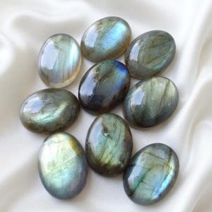 May include: A collection of nine polished, oval-shaped labradorite gemstones. Each stone features a smooth, reflective surface with iridescent flashes of blue, green, and gold light visible within the dark grey and brown mineral structure.