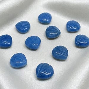 May include: Ten blue gemstone shell carvings are displayed. Each shell is intricately carved with lines, and the gemstones have a glossy finish. The shells are arranged on a white satin surface.