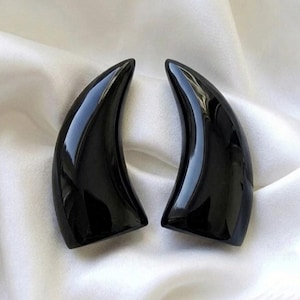 May include: A pair of smooth, polished black horn-shaped objects with a curved, tapered design. Each piece features a high-gloss finish that reflects light, creating a sleek, solid appearance with a wide base and a pointed, curved tip.