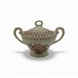 May include: Cream-colored ceramic sugar bowl with a lid and two handles. The bowl features a floral design with pink and green accents, and a brown patterned border around the lid. The lid has a small loop handle.