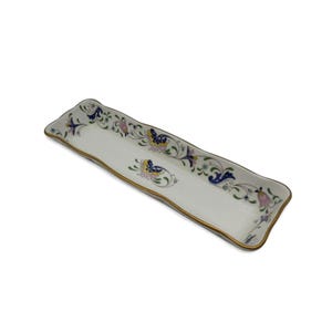 May include: A rectangular, white ceramic serving tray with a wavy edge and gold trim. The tray is decorated with a floral pattern in blue, yellow, pink, and green. The tray is ideal for serving appetizers or desserts.