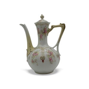 Może przedstawiać: Biały porcelanowy imbryk z kwiatowym wzorem różowych róż i zielonych liści. Imbryk posiada złocony uchwyt, długą wylewkę oraz pasującą pokrywkę. Dekoracyjne złote akcenty i małe czerwone detale zdobią korpus naczynia.