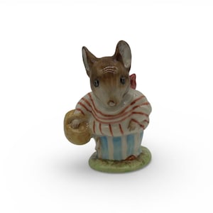 May include: A ceramic mouse figurine wearing a red and white striped top and blue striped skirt, holding a woven basket. The mouse has brown ears and a red bow. The figurine is on a green base.