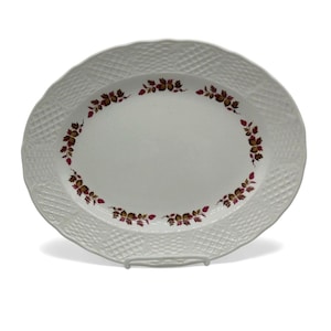 May include: White oval serving platter with a textured basketweave border. The center of the platter is plain white, and it is decorated with a floral pattern of brown and burgundy leaves. The platter is displayed on a white metal stand.