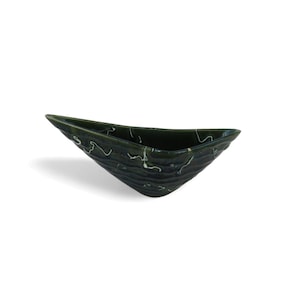 Puede incluir: Un cuenco de cerámica verde oscuro con forma triangular alargada y puntiaguda. El exterior presenta una superficie texturizada y ondulada con finas líneas blancas veteadas que recorren el esmalte oscuro, creando un contraste visual.