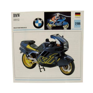 May include: A vintage BMW 1000 K1 motorcycle advertisement. The motorcycle is primarily dark blue with yellow accents on the wheels and body. The advertisement includes the BMW logo, the text "BMW 1000 K1", and the year 1988.