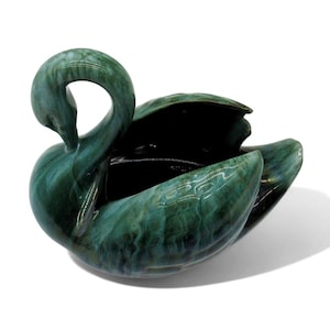 May include: A green glazed ceramic swan planter with a marbled finish. The swan has a long neck and a wide body with a hollow interior.