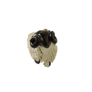May include: A ceramic sheep figurine with a cream-colored body and black horns and face. The sheep is facing forward, with its head slightly tilted. The figurine is set against a white background.