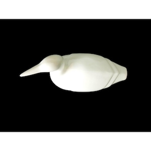 May include: A white duck figurine, carved with smooth lines and a long beak. The duck is set against a black backdrop, highlighting its form. This decorative item could be used as a home decor accent. The duck's measurements are in centimeters.