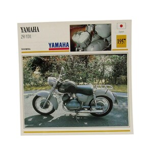 Może przedstawiać: Vintage reklama motocykla Yamaha 250 YD1 Touring przedstawiająca szary motocykl z czarnym zbiornikiem paliwa. Nadruk zawiera tekst YAMAHA 250 YD1, małe zdjęcie silnika, rok 1957 oraz ikonę japońskiej flagi w rogu.