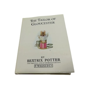 May include: A copy of "The Tailor of Gloucester" by Beatrix Potter. The book's cover shows a mouse reading a newspaper, sitting on a pink thread spool. The title is displayed above the illustration. Published by F. Warne & Co.