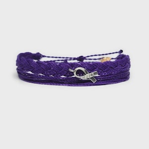 May include: A stack of purple bracelets. One bracelet is braided, and another has a silver ribbon charm with the word "HOPE" engraved on it. The bracelets are made of a woven material.