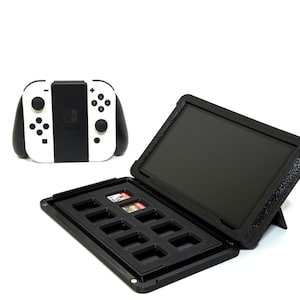 May include: A black and white Nintendo Switch controller is next to a black case with a screen and slots for game cartridges. The case is open, revealing several game cartridges. The case has a built-in stand.