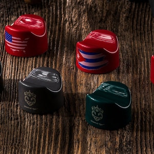 Puede incluir: Siete tapones de botella de cerámica de diferentes colores con un logotipo de león y un diseño de bandera en la parte superior. Los tapones están dispuestos sobre una superficie de madera.