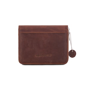 Puede incluir: Una cartera de cuero marr&oacute;n con cierre de cremallera. La cartera tiene una superficie texturizada y un peque&ntilde;o dije redondo sujeto por una cadena. El texto "Melia Games" est&aacute; grabado en la parte delantera. La cartera es rectangular.