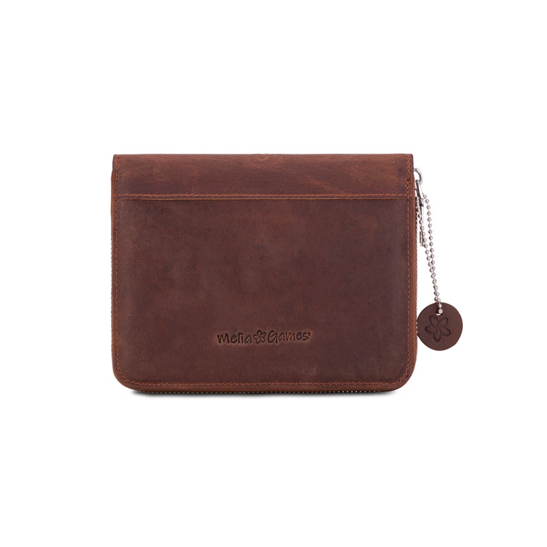 Puede incluir: Una cartera de cuero marr&oacute;n con cierre de cremallera. La cartera tiene una superficie texturizada y un peque&ntilde;o dije redondo sujeto por una cadena. El texto "Melia Games" est&aacute; grabado en la parte delantera. La cartera es rectangular.