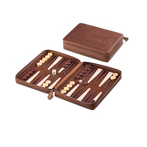 Könnte beinhalten: Ein Backgammon-Set aus braunem Leder, geöffnet, um das Spielbrett mit braunen und weißen Dreiecken zu zeigen. Das Set enthält braune und cremefarbene Spielsteine, Würfel und eine Reißverschlusstasche. Die geschlossene Tasche ist ebenfalls aus braunem Leder.