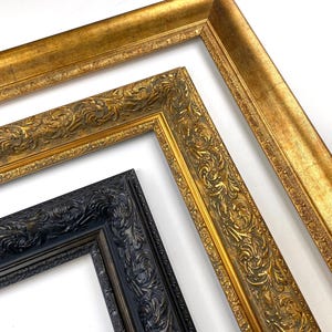 Puede incluir: Tres marcos de fotos ornamentados en oro y negro. Los marcos dorados tienen detalles de volutas y un acabado metálico. El marco negro tiene un diseño similar. Los marcos están en ángulo, mostrando sus bordes decorativos.