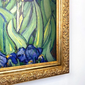 Puede incluir: Impresi&oacute;n enmarcada de una pintura con lirios. La obra presenta lirios azules y morados con hojas verdes, sobre un fondo de pinceladas verdes y amarillas. La pintura est&aacute; encerrada en un marco dorado y ornamentado.