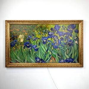 Puede incluir: Una impresi&oacute;n enmarcada de la pintura "Lirios" de Vincent van Gogh. La obra presenta vibrantes lirios azules con hojas verdes, sobre un fondo de jard&iacute;n. El marco es ornamentado, con un acabado dorado.