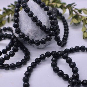 May include: A close-up of a black beaded necklace. The beads are round and smooth, and the necklace is lying on a white surface.