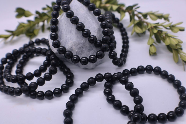 May include: A close-up of a black beaded necklace. The beads are round and smooth, and the necklace is lying on a white surface.