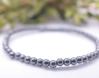 May include: A black hematite beaded bracelet with a simple design. The bracelet is made of small, round beads that are strung together on a thin cord.